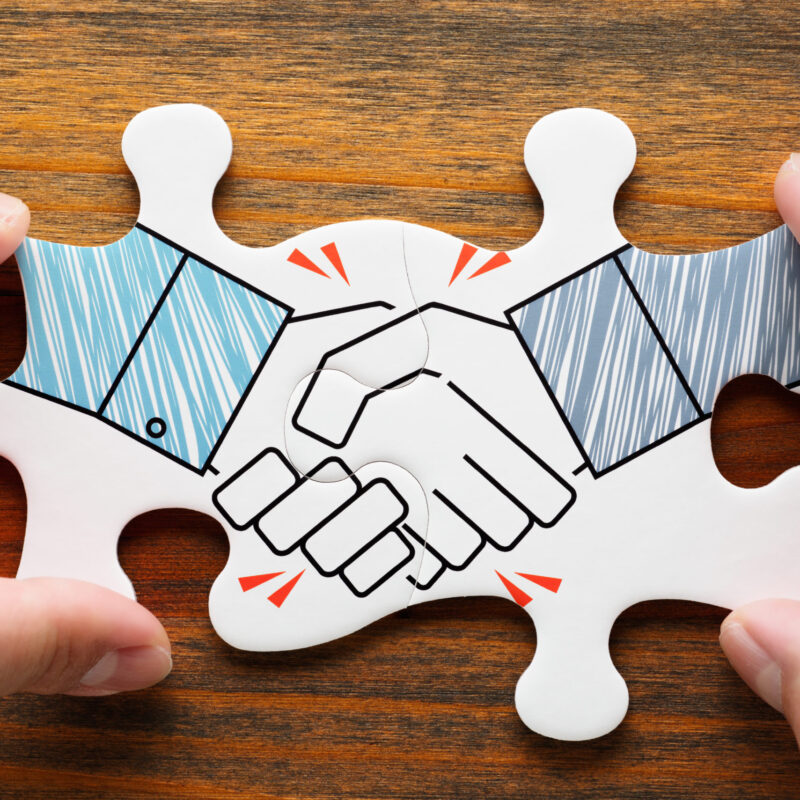 two puzzle pieces fitting together revealing a handshake