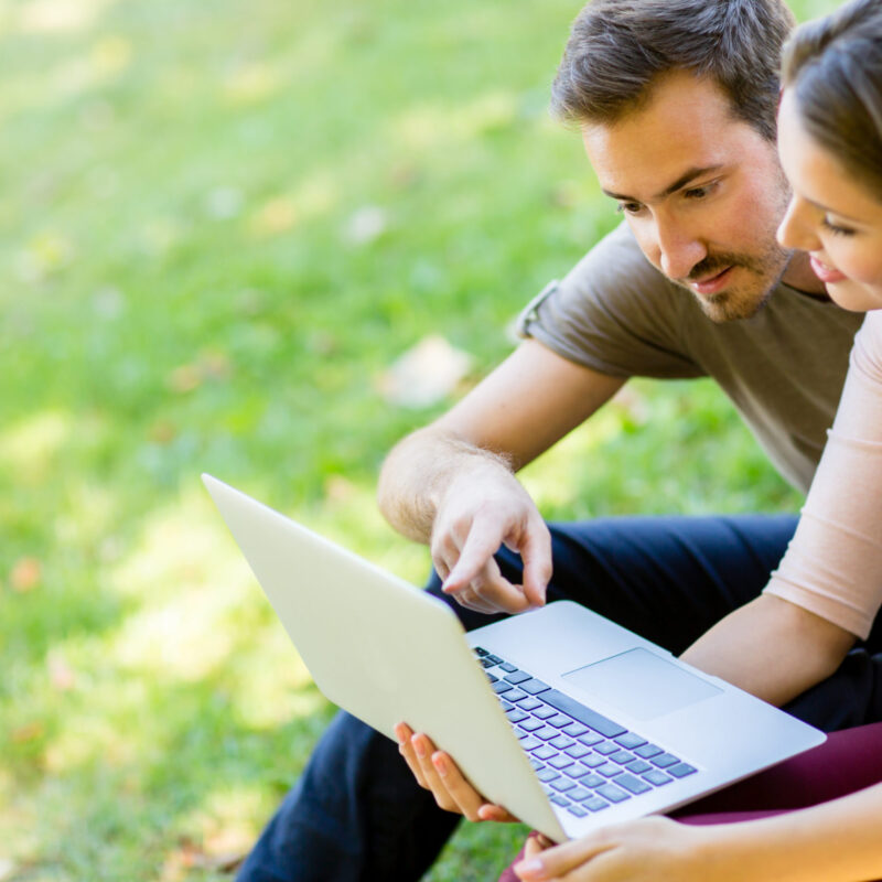 man and woman looking at laptop in park