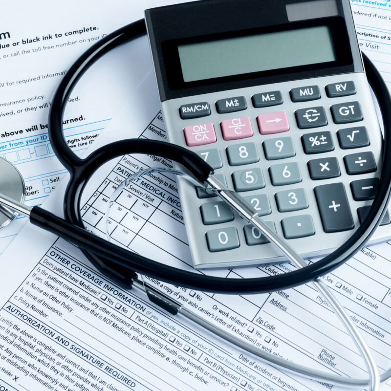 calculator and stethoscope on pile of bills
