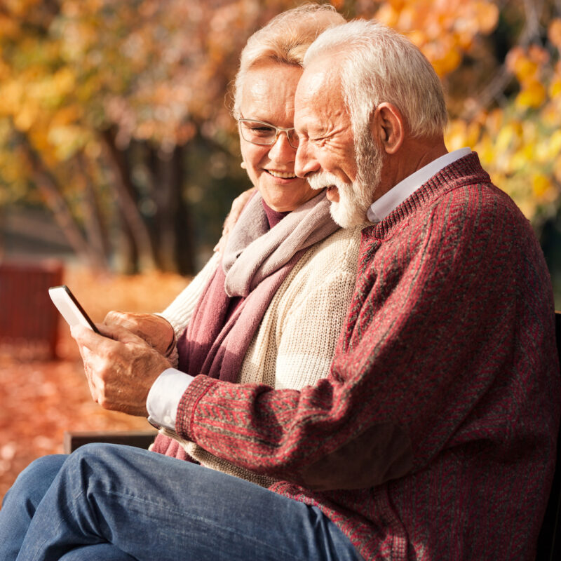 senior couple on bench looking at smartphone